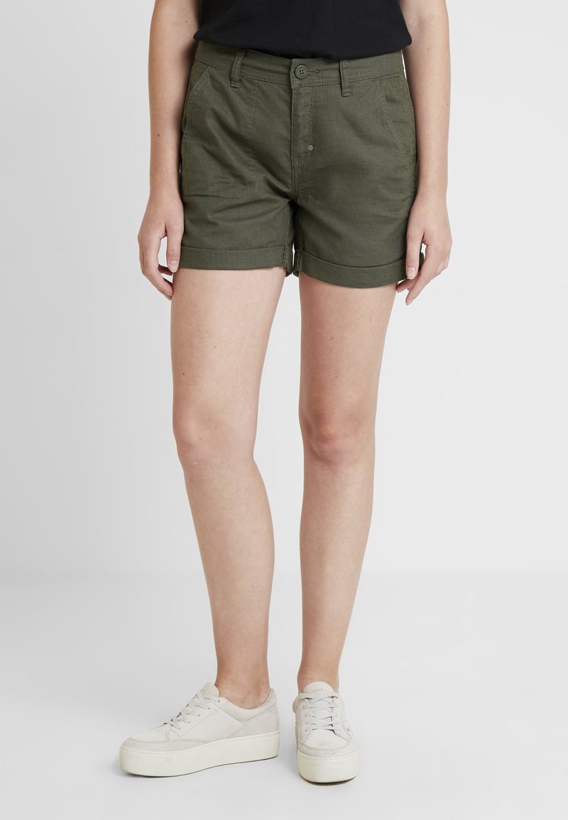 Green cotton shorts with a fitted design, rolled cuffs, front pockets, and a button closure. Paired with light-colored platform shoes.