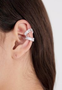 Silberner Ohr-Clip mit geschwungener Form, der rechteckige Akzentstücke aufweist und am Ohr getragen wird. Glatte Textur mit metallischem Finish.