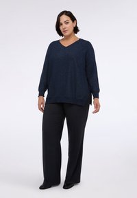 Maglione a collo a V in maglia blu navy scintillante; abbinato a pantaloni scuri. Vestibilità ampia con spacchi laterali; tessuto liscio e maniche lunghe.