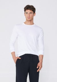 Weißes Langarm-T-Shirt mit Rundhalsausschnitt, kombiniert mit schwarzen Sweatpants mit Kordelzug. Der Stoff scheint weich zu sein und das Design hat eine lockere Passform.