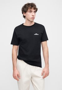 Μαύρη βαμβακερή μπλούζα με κοντά μανίκια, με μικρό λευκό λογότυπο "OBTY WORLDWIDE" στο αριστερό μέρος του στήθους. Κανονική εφαρμογή.