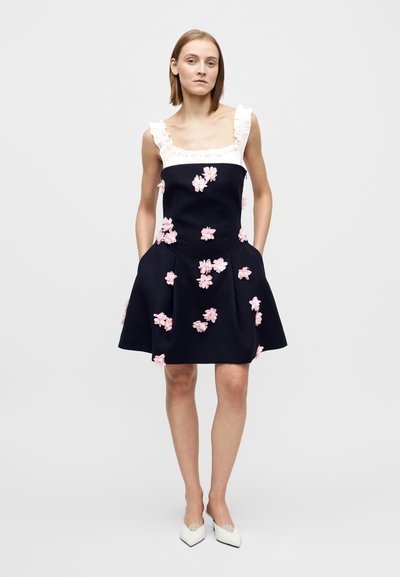 Abito blu navy ricamato con fiori e scollatura bianca con volant, dotato di tasche e decorato con fiori di stoffa rosa sul corpetto e sulla gonna.