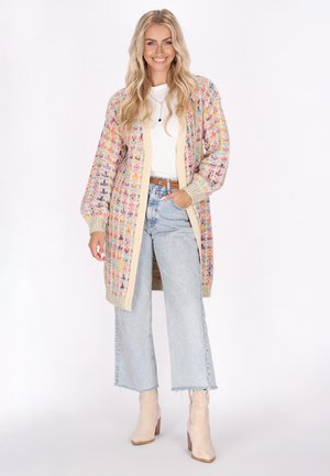 Cardigan tricotat în culori pastel cu un model geometric, margine bej, deschis în față și mâneci lungi. Purtați peste o cămașă albă și blugi cu talie înaltă.