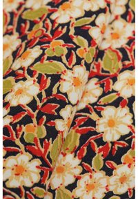 Tessuto floreale con fiori giallo-bianchi accentati di rosso e foglie verdi su uno sfondo blu scuro, che presenta un motivo tessuto e strutturato.