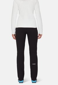 Svarta softshellbyxor med en åtsittande design, tillverkade av slitstarkt material. Har en söm vid knäet och en vit logotyp på underbenet.
