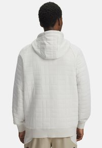Hoodie blanc rembourré avec une texture matelassée, capuche ajustable, poignets côtelés et détails de surpiqûre contrastants. Design simple et moderne.