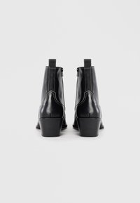 Botas de tobillo de cuero negro con puntera redondeada, tacón cuadrado, costuras visibles y cremalleras en los laterales. Textura suave con un acabado mate.