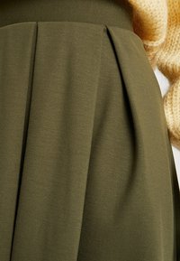 Olivgrön plisserad kjol gjord av mjukt tyg, med en slät yta och strukturerad midja, som framhäver rena linjer och minimal design.