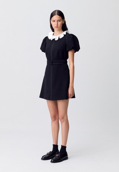 Vestido corto negro con mangas abullonadas y cuello blanco con volantes, cintura ajustada con un cinturón, costuras detalladas, combinado con mocasines y calcetas.