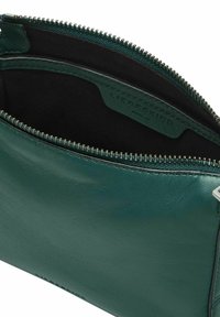 Zielony skórzany woreczek z srebrnym zamkiem błyskawicznym, posiadający miękką podszewkę wewnętrzną i wytłaczaną metkę marki, o prostokątnym kształcie i gładkiej teksturze.