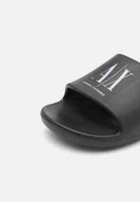 Sorte slidesandal med åben tå-design, lavet af glat gummi materiale, med hvid "AX" logo og tekstureret inderside for greb.