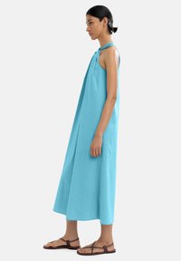 Turkusowa sukienka bez rękawów o luźnym kroju, sięgająca do kolan, z węzłowymi ramiączkami. Połączona z brązowymi płaskimi sandałami.