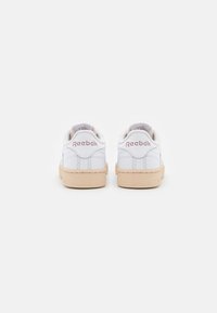 Baskets Reebok blanches avec une tige en cuir lisse, logo rose et semelle en caoutchouc beige. Présente un design épuré et un col rembourré.