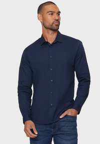 Marineblauwe overhemd met lange mouwen en een button-down kraag, voorzijde met knopen en een subtiele logo op de borst; gladde stof en een getailleerde pasvorm.