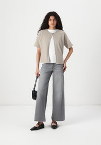 Beige, kortermet genser med knappelukking, sammen med høy midje grå vide jeans og svarte leiligheter med dekorative aksenter.