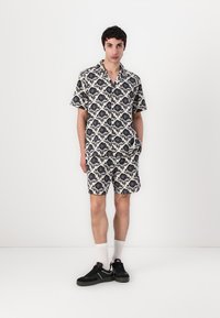 Kortærmet skjorte med krave og matchende shorts i cremekulør med et mørkt blomstermønster. Båret med sorte sneakers og hvide ankelsokker.