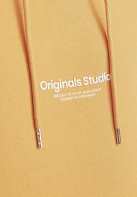 Gele sweatshirt met een zachte textuur, voorzien van witte bedrukte tekst "Originals Studio" en zilverkleurige trekkoorden.