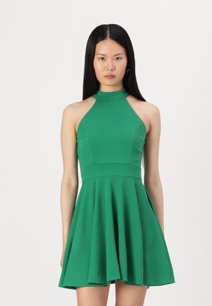 Robe débardeur verte avec un corsage ajusté et une jupe évasée, fabriquée dans un tissu lisse et extensible. Présente un col haut et une longueur jusqu'au mi-cuisse.