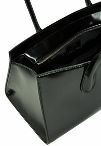 Borsa in pelle verniciata nera con forma strutturata, due manici e una tasca interna con cerniera. Interno foderato con dettagli di cucitura.