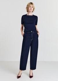 Marineblaue T-Shirt mit kurzen Ärmeln und weißen Nähten, kombiniert mit hochtaillierter, dunkelblauer, weiter Jeanshose und burgunderroten Absätzen.