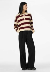 Vīnogas sarkana un krēmkrāsas svītrotā džemperis ar apkakli un trim pogām, kopā ar melnām plānu svītru platām biksēm un tumšiem apaviem.