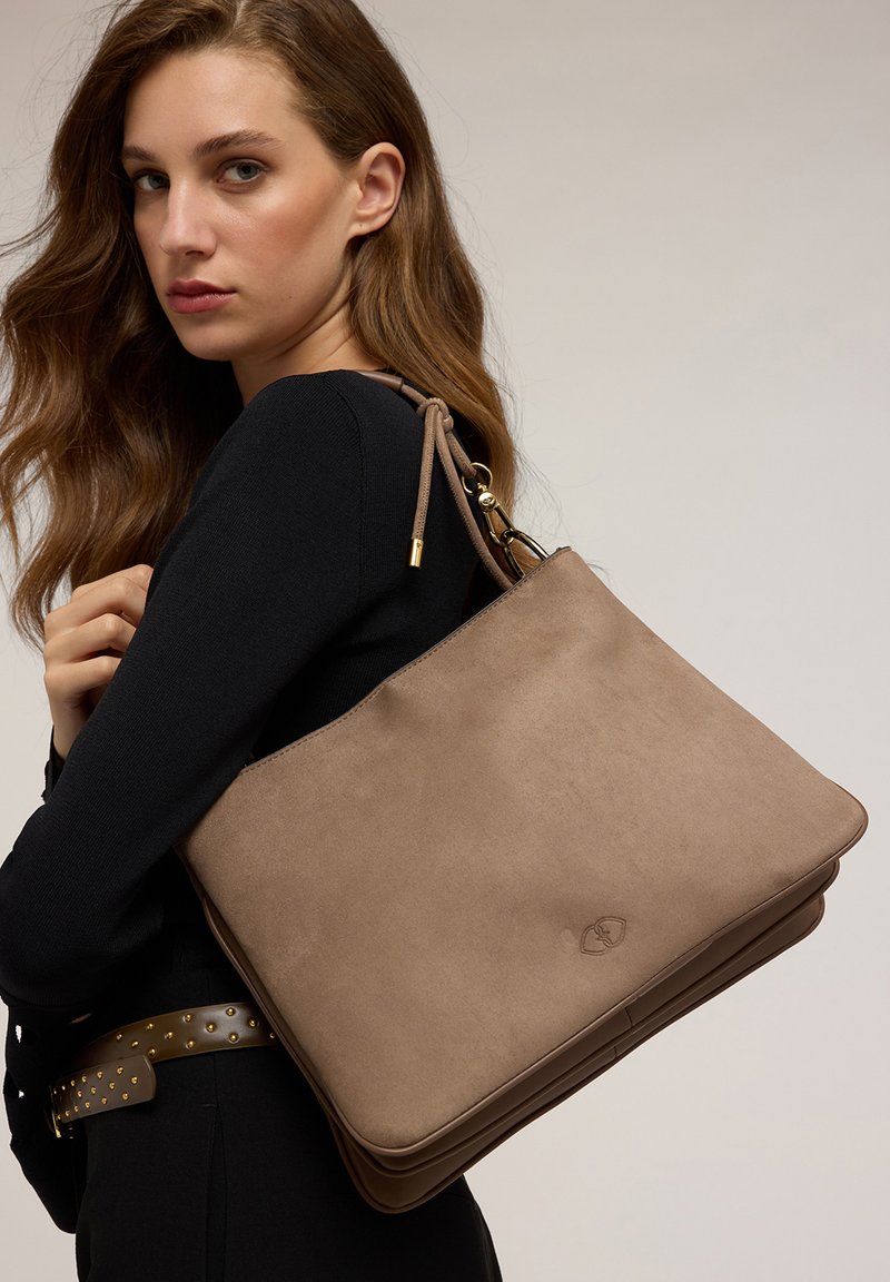 Sac à épaule en suède beige avec une texture lisse, mettant en avant un accent en métal doré et un design minimaliste. Forme rectangulaire lisse.