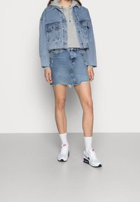 Džínová bunda s crop střih, šedá mikina pod ní a modrá džínová sukně. Bílé tenisky Nike s modrými a červenými akcenty.