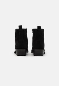 Stivali ankle in suede nero con tacco basso e impilato, dotati di cerniere laterali e linguette per una facile indossabilità. Texture liscia con un design minimalista.