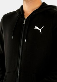 Felpa nera con zip, realizzata in tessuto morbido, dotata di tasca a marsupio e di un logo Puma bianco sulla parte sinistra del petto.