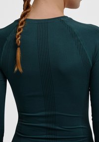 Sportieve T-shirt met lange mouwen in donkergroen, met een gladde textuur, slim fit en een subtiel geperforeerd streepjespatroon langs de achterkant.