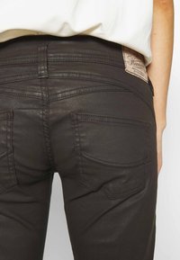 Jean noir slim avec une texture lisse, doté de deux poches arrière, d'une couture distincte et d'une étiquette de marque sur la ceinture.