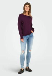Pull en tricot violet avec un décolleté bateau et des manches longues, associé à un jean skinny déchiré bleu clair et des mocassins noirs.