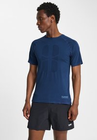 Marinblå kortärmad träningströja med en texturerad logotyptryck på framsidan, rund halsringning och kontrasterande sömmar. Bärs med svarta shorts.