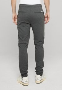 Pantaloni da jogging grigi in tessuto morbido, con design affusolato, vita elastica e due tasche posteriori, abbinati a sneaker bianche e grigie.