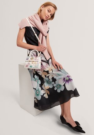 Bloemenjurk met zwarte achtergrond, voorzien van grote lichtblauwe en paarse bloemen. Geaccentueerd met een lichtroze gebreide sjaal en een decoratieve handtas.