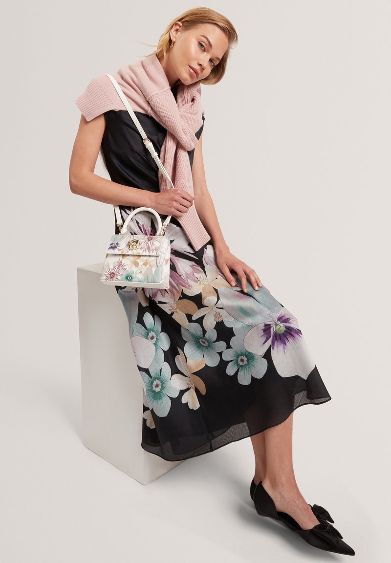 Blumenkleid mit schwarzem Hintergrund, versehen mit großen hellblauen und violetten Blumen. Akzentuiert mit einem blassrosa gestrickten Schal und einer dekorativen Handtasche.