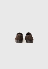 Mocassins en daim marron foncé avec un profil bas, un bout rond et une semelle en caoutchouc noir lisse. Détail de couture unique le long du talon.