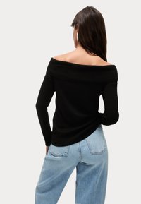 Czarny sweter typu off-the-shoulder z prążkowanej tkaniny, dopasowany krój, w połączeniu z jasnoniebieskimi spodniami z wysokim stanem, widoczne szwy z tyłu.