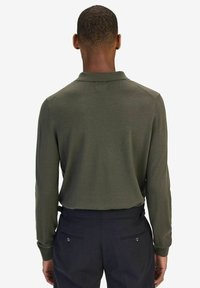 Donkergroene gebreide polo met lange mouwen en een kraag, met een gestructureerde afwerking en aangesloten manchetten, gedragen met donkere broeken.