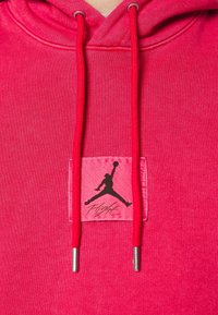 Sweat à capuche rose vif avec cordons rouges et un écusson carré représentant une silhouette noire de joueur de basketball et le mot "Flight".