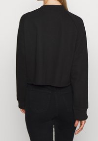 Black cropped sweatshirt made of soft fabric, with ribbed collar and long sleeves. Pair with high-waisted black jeans visible on the back.