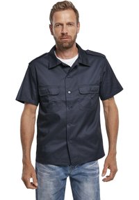 Camicia azzurra a maniche corte con bottone, dotata di due tasche frontali e spalline. Tessuto testurizzato con una vestibilità strutturata.
