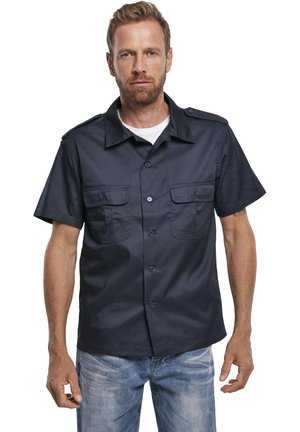 Camisa de botones de manga corta en azul marino con dos bolsillos frontales y epaulettes en los hombros. Tejido texturizado con un ajuste estructurado.