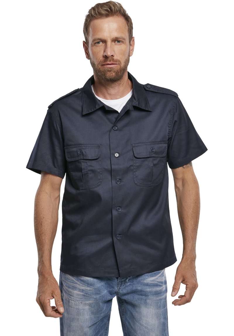 Camicia azzurra a maniche corte con bottone, dotata di due tasche frontali e spalline. Tessuto testurizzato con una vestibilità strutturata.