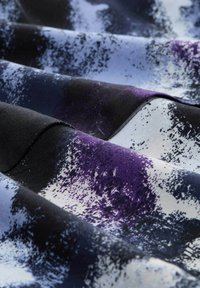 Tessuto caratterizzato da un tessuto liscio con una combinazione di colori nero, viola e bianco, che presenta un motivo astratto e texturizzato.