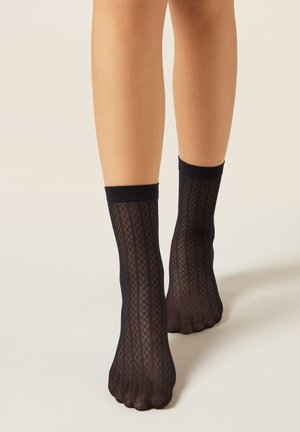Calzini alla caviglia neri con motivo a rombi e polsino solido. Realizzati in materiale trasparente, aderiscono perfettamente alla caviglia.