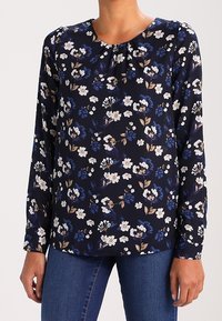 Blusa floreale navy con maniche lunghe, con motivi di fiori bianchi e blu, scollatura leggermente arricciata e tessuto leggero.