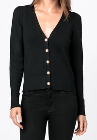 Svart kardiagan med djup V-ringning, långa ärmar och dekorerande guldknappar. Tillverkad av ett mjukt material med en åtsittande design.