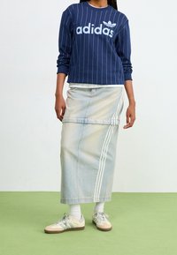 Navy striped sweatshirt with "adidas" logo, light blue denim skirt with vertical white stripes, and beige sneakers with blue accents.