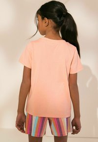 Pfirsichfarbene Baumwoll-T-Shirt mit kurzen Ärmeln, kombiniert mit bunten gestreiften Shorts, die aus mehreren lebhaften Farben und einer weichen Textur bestehen.